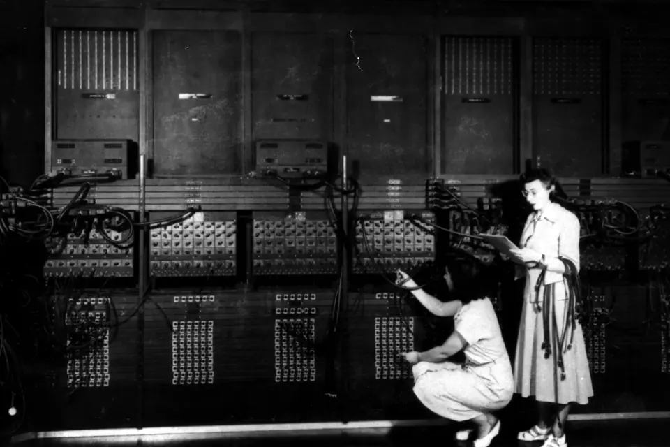 Two women programmers set up the wiring panels of the room-sized ENIAC computer in a black-and-white photograph