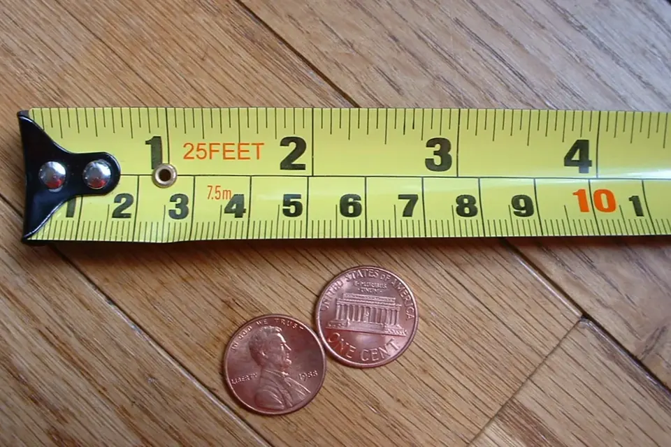 A yellow tape measure marked in feet and centimetres lying on a wooden floor next to two copper coins